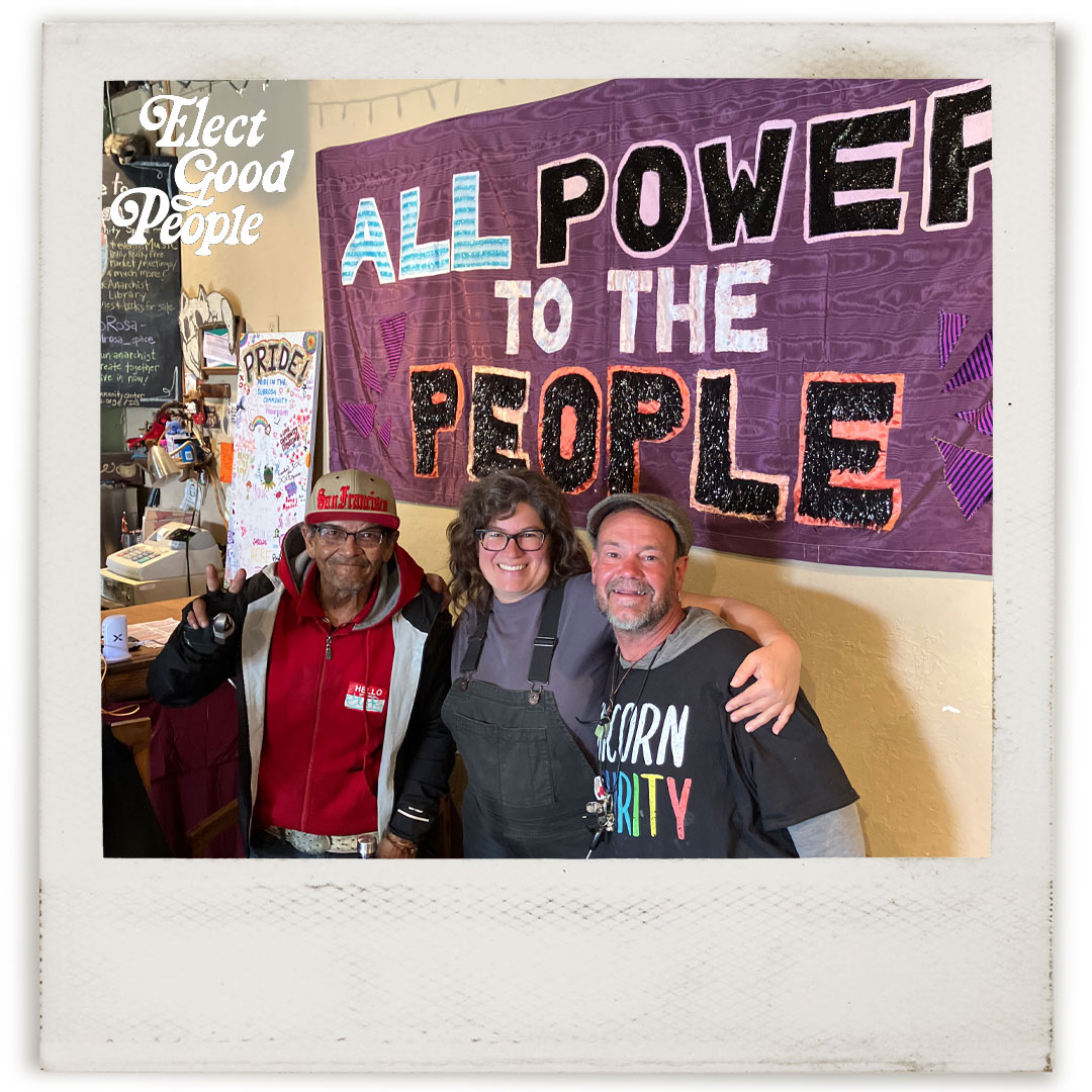 Candidate Joy Schendledecker poses with friends in front of a sign that reads, "All power to the people."